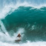Wetsuit - Male surfer in water suit riding surfboard on powerful blue wave while practicing extreme sport