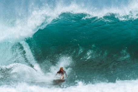 Wetsuit - Male surfer in water suit riding surfboard on powerful blue wave while practicing extreme sport