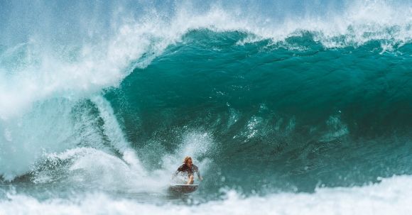 Wetsuit - Male surfer in water suit riding surfboard on powerful blue wave while practicing extreme sport