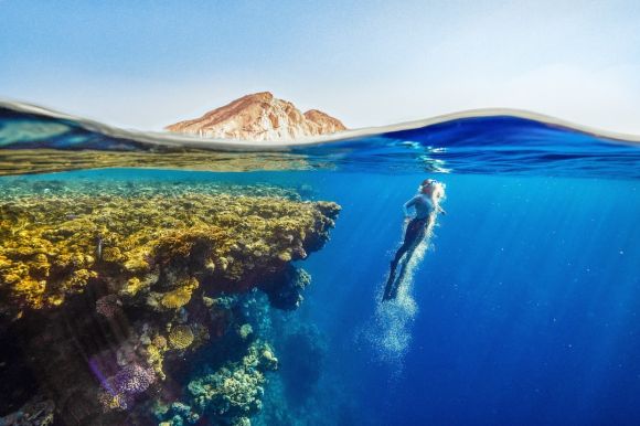 Diving Locations - a person swimming in the ocean with a mountain in the background