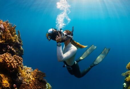 Diving Locations - a woman scubas in the ocean with a camera