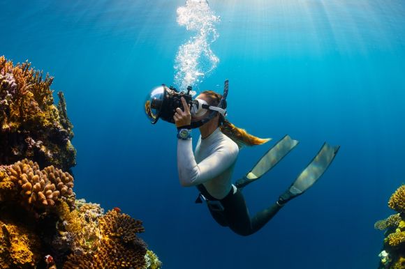 Diving Locations - a woman scubas in the ocean with a camera