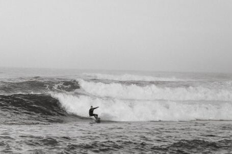 Wetsuit - Black and white side view of anonymous sportsman on surfboard practicing extreme sport on foamy ocean