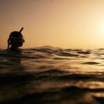 Diving Locations - a person swimming in the ocean at sunset