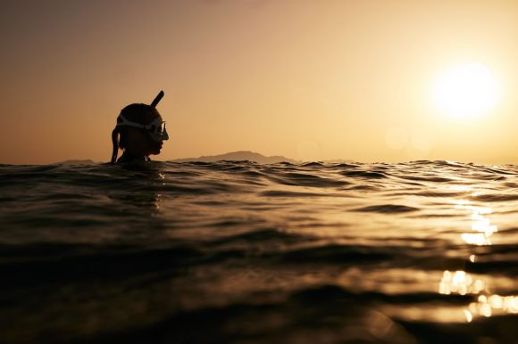 Diving Locations - a person swimming in the ocean at sunset