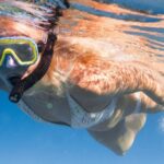 Snorkel - Full length of faceless female diving underwater in bikini and flippers with snorkeling mask in clear blue water