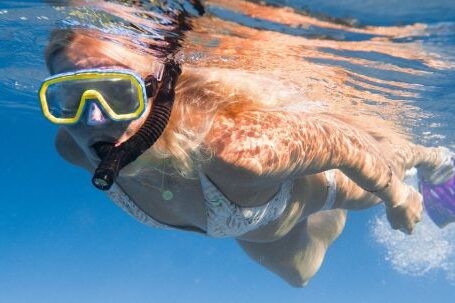 Snorkel - Full length of faceless female diving underwater in bikini and flippers with snorkeling mask in clear blue water