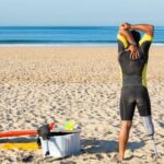 Wetsuit - Faceless amputee man stretching body on beach before surfing
