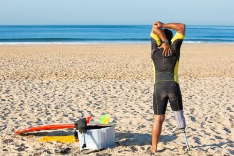 Wetsuit - Faceless amputee man stretching body on beach before surfing