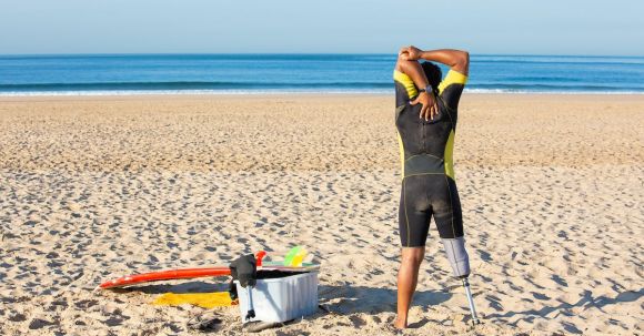 Wetsuit - Faceless amputee man stretching body on beach before surfing