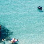 Snorkeling - Man and Woman Swimming in the Sea Near Brown Cliff