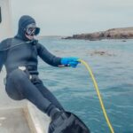 Scuba Diving - Person in Scuba Diving Gear Sitting on a Boat Holding a Yellow Hose