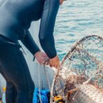 Scuba Diving - A Scuba Diver Fixing a Mesh Net Aboard a Boat