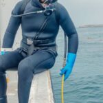 Scuba Diving - Man in Wetsuit Sitting on a Boat Holding a Hose