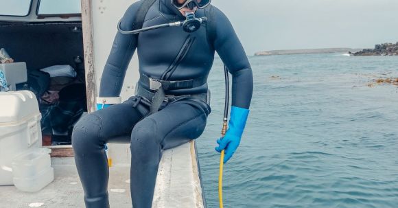 Scuba Diving - Man in Wetsuit Sitting on a Boat Holding a Hose