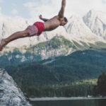 Diving - Man Wearing White and Red Board Short Diving from Rock Formation