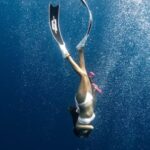 Snorkel - Anonymous female diver swimming under blue ocean in sunlight