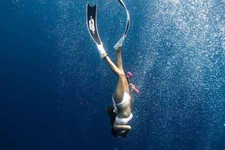 Snorkel - Anonymous female diver swimming under blue ocean in sunlight