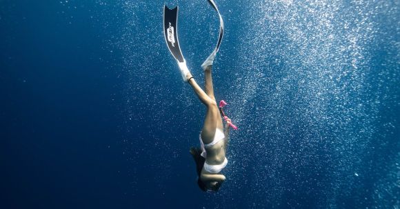 Snorkel - Anonymous female diver swimming under blue ocean in sunlight