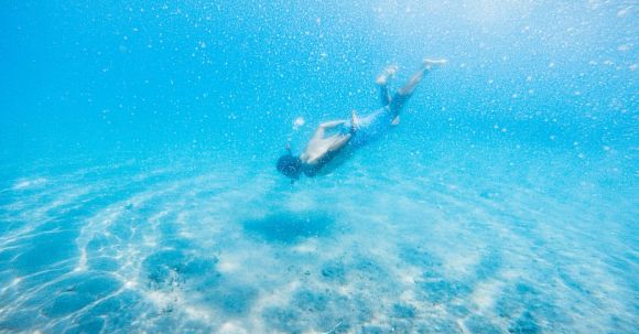 Diving Mask - Anonymous male diver swimming in bright blue water during vacation