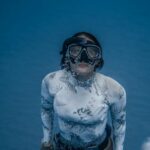 Wetsuit - From above of anonymous female diver in flippers wearing white swimsuit rising from deep water with bubbles in sea
