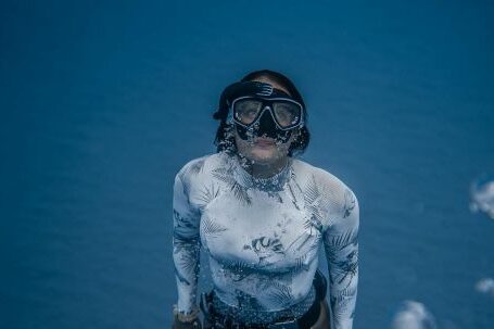 Wetsuit - From above of anonymous female diver in flippers wearing white swimsuit rising from deep water with bubbles in sea