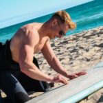 Wetsuit - Man Waxing Surfboard on Beach