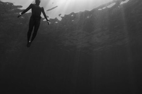 Wetsuit - Black and white of from below of scuba diver swimming in clear water in swimsuit under rays of light