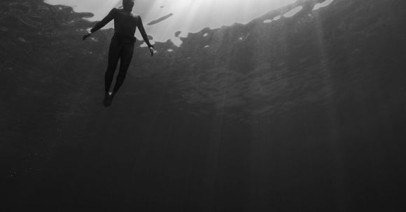 Wetsuit - Black and white of from below of scuba diver swimming in clear water in swimsuit under rays of light
