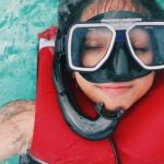 Snorkel - A person wearing red and black life vest and goggles while swimming