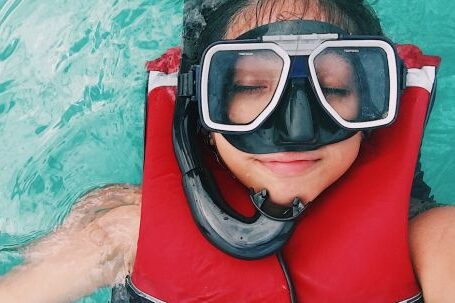 Snorkel - A person wearing red and black life vest and goggles while swimming