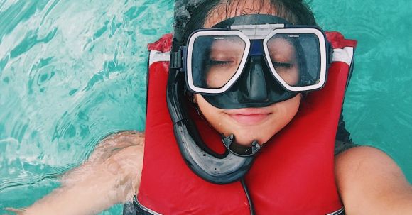 Snorkel - A person wearing red and black life vest and goggles while swimming
